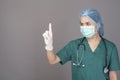 Young confident woman doctor in green scrubs is wearing surgical mask over grey background studio Royalty Free Stock Photo