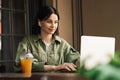 Young Confident Woman Using Earphones and Laptop While Sitting at a Cafe Table, Brunette Girl Working at Restaurant With Royalty Free Stock Photo