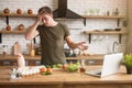 Young confused man standing in well-equipped kitchen has no idea what to cook for breakfast looking desperate checking recipe in Royalty Free Stock Photo