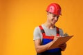 Young construction worker wearing hardhat and holding a clipboard on yellow background in studio Royalty Free Stock Photo