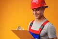 Young construction worker wearing hardhat and holding a clipboard on yellow background in studio Royalty Free Stock Photo