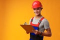 Young construction worker wearing hardhat and holding a clipboard on yellow background in studio Royalty Free Stock Photo