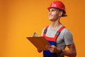 Young construction worker wearing hardhat and holding a clipboard on yellow background in studio Royalty Free Stock Photo