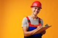 Young construction worker wearing hardhat and holding a clipboard on yellow background in studio Royalty Free Stock Photo