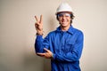 Young constructor man wearing uniform and security helmet over isolated white background smiling with happy face winking at the Royalty Free Stock Photo