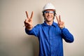 Young constructor man wearing uniform and security helmet over isolated white background smiling looking to the camera showing Royalty Free Stock Photo