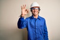 Young constructor man wearing uniform and security helmet over isolated white background smiling positive doing ok sign with hand Royalty Free Stock Photo