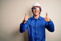 Young constructor man wearing uniform and security helmet over isolated white background success sign doing positive gesture with Royalty Free Stock Photo