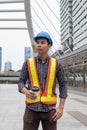 Young constructor with safety helmet in work vest holding coffee cup in construction site