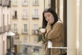 Young contemplative and beautiful Asian woman at home or hotel balcony - thoughtful Chinese girl having morning coffee enjoying