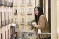 Young contemplative and beautiful Asian woman at home or hotel balcony - thoughtful Korean girl having morning coffee enjoying