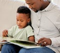 Young content African american father reading a book with his son sitting on the couch at home. Little boy enjoying a Royalty Free Stock Photo