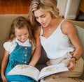 Young content caucasian mother and little daughter reading a story book together sitting on the couch at home. Carefree Royalty Free Stock Photo