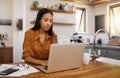 Young content mixed race businesswoman going through paper and bills while typing on a laptop at home. Serious hispanic