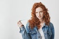 Young cool brutal redhead girl in jean jacket chewing gum looking at camera over white background.