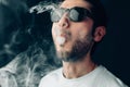 Young cool guy in sunglasses exhales a cloud of smoke. Studio horizontal portrait in close-up. Royalty Free Stock Photo