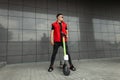 Young cool man hipster posing with electric scooter. Guy in fashionable red- black jeans clothes in sunglasses with a scooter Royalty Free Stock Photo