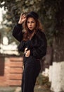 Young cool teen hipster woman looking serious near the tree on the street background in black style clothing, jeans, jacket and