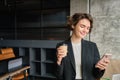 Young corporate woman, saleswoman in office, drinks her morning coffee and reads messages on mobile phone, working Royalty Free Stock Photo