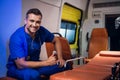 Young corpsman in blue medical uniform sits in the ambulance car and smiles
