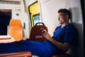 Young corpsman in blue medical uniform sits with phone in his hands in the ambulance car