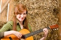 Young country woman playing guitar in barn