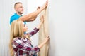 Young Couple Applying Wallpaper On Wall