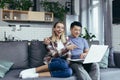 Young couple Asian man and woman at home sitting on sofa together using laptop, happy and smiling multiracial family looking at Royalty Free Stock Photo