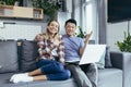 Young couple Asian man and woman at home sitting on sofa together using laptop, happy and smiling multiracial family looking at Royalty Free Stock Photo