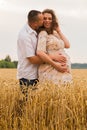 Young couple awaiting baby embrace the field