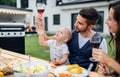 Young couple with baby sitting at table outdoors on family garden barbecue. Royalty Free Stock Photo