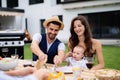 Young couple with baby sitting at table outdoors on family garden barbecue. Royalty Free Stock Photo