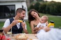 Young couple with baby sitting at table outdoors on family garden barbecue. Royalty Free Stock Photo