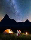 Young couple backpackers sitting together under starry sky near campfire and shines tent at night Royalty Free Stock Photo