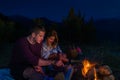 Young couple baking sausages on the campfire and drinking beer in the forest hill in the dusk