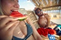 Young couple at beach eating watermelon. Man and woman laying on sunbeds enjoying vacation together. Holiday, fun, lesiure,
