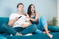 Young couple beautiful brunette woman and handsome man watching movie on the sofa eating pop corn looking surprised cozy Royalty Free Stock Photo