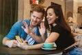 Young couple beautiful woman and handsome man having online conversation with friends in the cafe drinking hot coffee looking Royalty Free Stock Photo