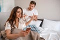 Young couple in the bed. Indifferent busy woman with phone is ignoring her irritated man with gift, begging for