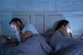 Couple in bed on mobile phones ignoring each other in relationship problems and technology addiction Royalty Free Stock Photo