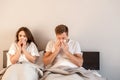 Young couple in the bed. Sick man and woman are blowing noses and suffering from ill in the bedroom Royalty Free Stock Photo