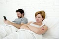 young couple in bed unsatisfied wife bored frustrated and angry while internet addict husband is using mobile phone social networ