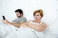 young couple in bed unsatisfied wife bored frustrated and angry while internet addict husband is using mobile phone social networ