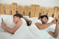 Young couple in bed using mobile phone lying backs to each other, relationship and communication problems