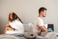 Young couple in the bedroom. Unhappy man and woman are sitting back to back in the bed, couple quarrel home scene Royalty Free Stock Photo