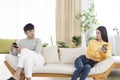 Young couple being in quarrel and not talking.Sitting in living room.Using smartphone Royalty Free Stock Photo