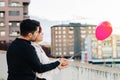 Young couple, boy and girl, with their backs turned and unrecognizable, holding a red heart-shaped balloon on a balcony with the Royalty Free Stock Photo