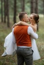 Young couple bride in a white short dress and groom in a gray suit in a pine forest