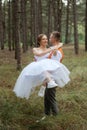 young couple bride in a white short dress and groom in a gray suit in a pine forest