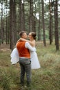 young couple bride in a white short dress and groom in a gray suit in a pine forest